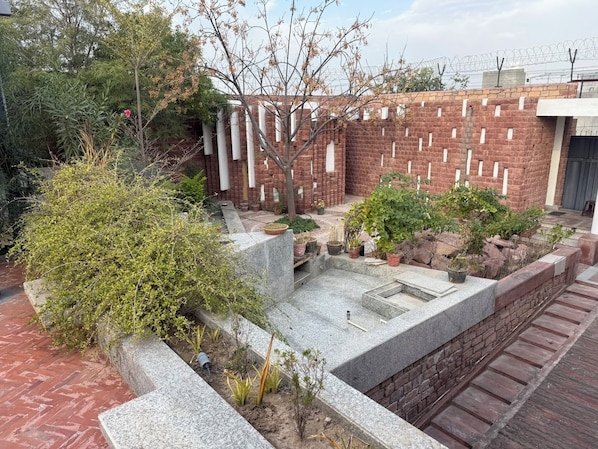 A courtyard with a brick wall, potted plants, and a stone bench.