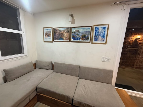 Un salon avec un canapé d’angle, une fenêtre et quatre tableaux encadrés accrochés au mur.