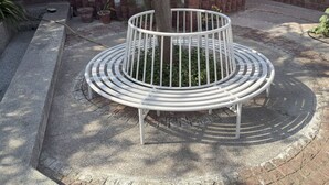 Un banco de metal circular con un árbol en el centro, rodeado por un sendero de ladrillo.