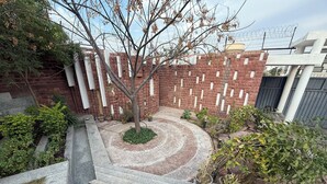 Une cour avec un mur en briques, un arbre, des plantes en pot et un banc en bois.