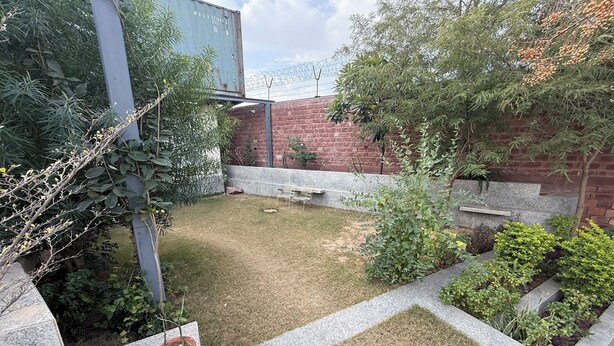 Un patio trasero con césped, un muro de ladrillo y diversas plantas.