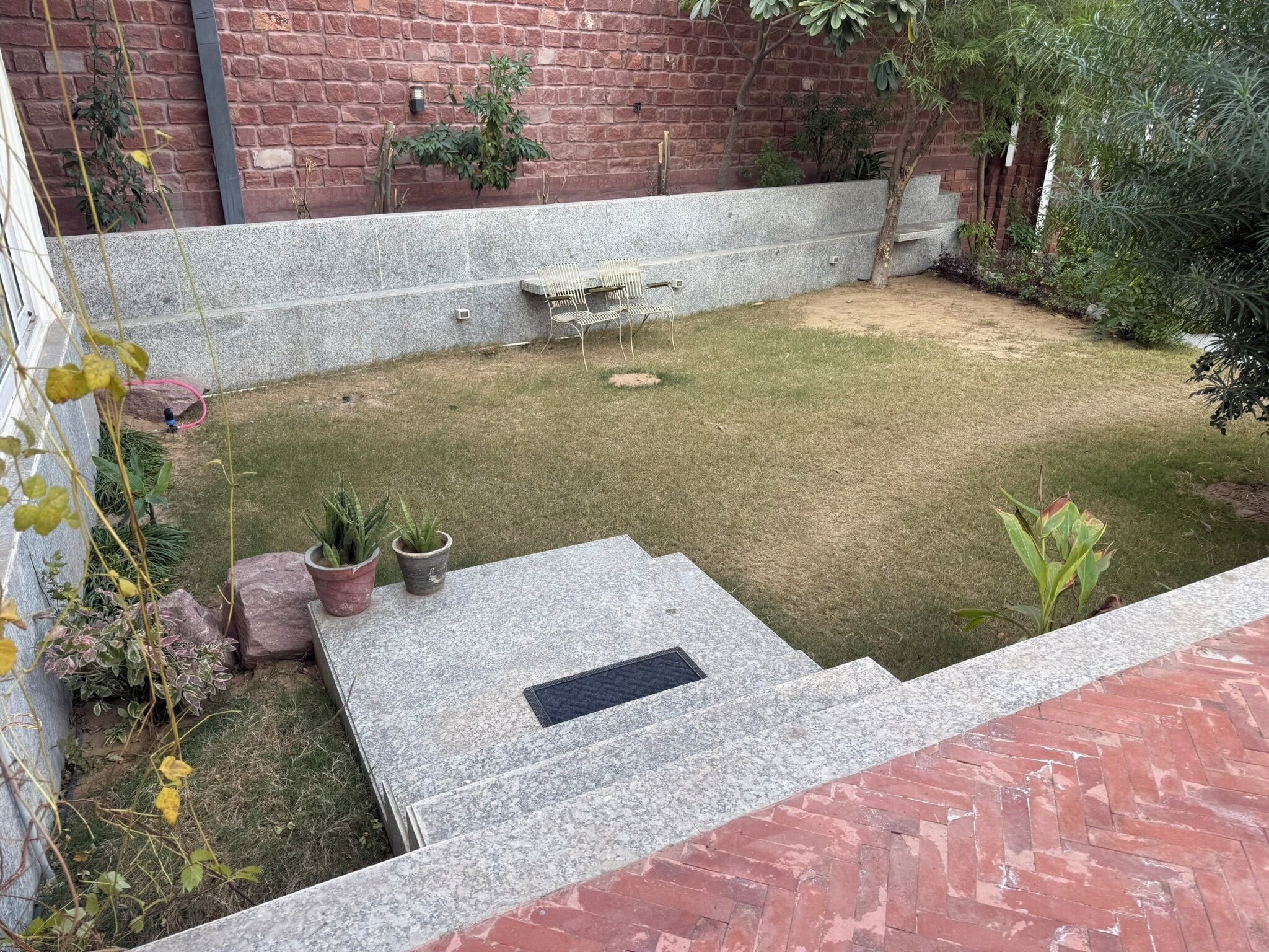 A courtyard with a brick wall, a stone bench, and potted plants.