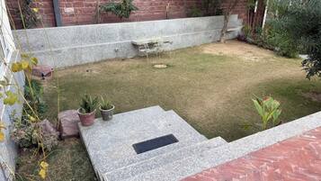 A courtyard with a brick wall, a stone bench, and potted plants.