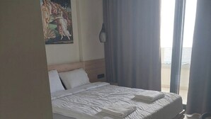 Quarto de hotel com uma cama grande, um quadro na parede e vista para o mar pela janela.