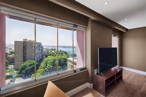 A modern living room with a large window, a flat-screen TV, and a wooden entertainment unit. - Vesta - Luxury Nile View APT - 2BR - Maadi II (Cairo)