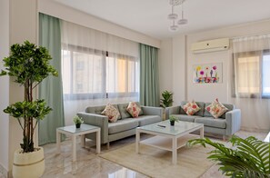 A modern living room with a grey sofa, two side tables, a glass coffee table, and a large potted plant. - Vesta - Luxury APT - 3BR - Sheikh Zayed I (Sheikh Zayed City)