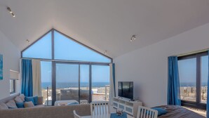 Un salon moderne comprenant un coin repas, de grandes fenêtres, un téléviseur à écran plat et une vue sur la mer.