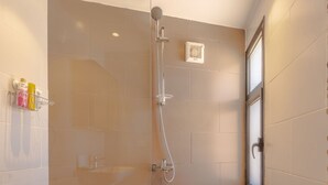 Un espace douche fermé par des parois de verre, avec un sol carrelé et une fenêtre sur le côté droit.