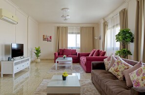 A living room with a flat-screen TV, a white coffee table, a red sofa, and a brown sofa with floral cushions. - Vesta - Luxury APT - 3BR - Sheikh Zayed II (Sheikh Zayed City)
