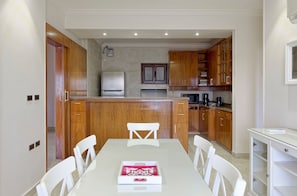A modern kitchen with wooden cabinets, a stainless steel refrigerator, and a dining area with a white table and chairs. - Vesta - Luxury APT - 3BR - Sheikh Zayed II (Sheikh Zayed City)