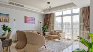 A modern living room with a beige sofa, a matching armchair, a coffee table, and a large window with curtains. - Vesta - Luxury Apt - 3BR - CFC Xlii (New Cairo)