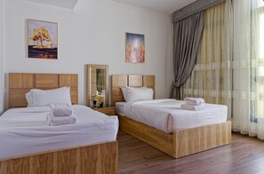 Ett hotellrum med två sängar i trä, vita sängkläder och ett stort fönster med gardiner.