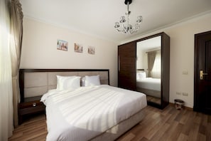 A hotel room with a large bed, a wooden floor, a chandelier, and a mirror. - Vesta - Luxury APT - 3BR - Mohandessin II (Giza)