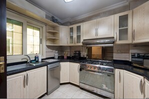 A kitchen with light wooden cabinets, a stainless steel stove, and a dishwasher. - Vesta - Luxury APT - 3BR - Mohandessin II (Giza)
