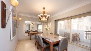 A dining area with a marble table, grey chairs, a chandelier, and a large window with a view of the city. - Vesta- Luxury Panoramic Duplex - 3br- Zamalek II (Cairo)