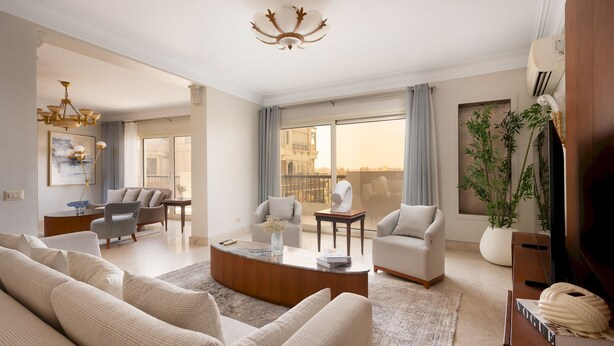 A spacious living room with a large sofa set, a round coffee table, and a chandelier. There are multiple seating areas with chairs and a dining table. - Vesta- Luxury Panoramic Duplex - 3br- Zamalek II (Cairo)