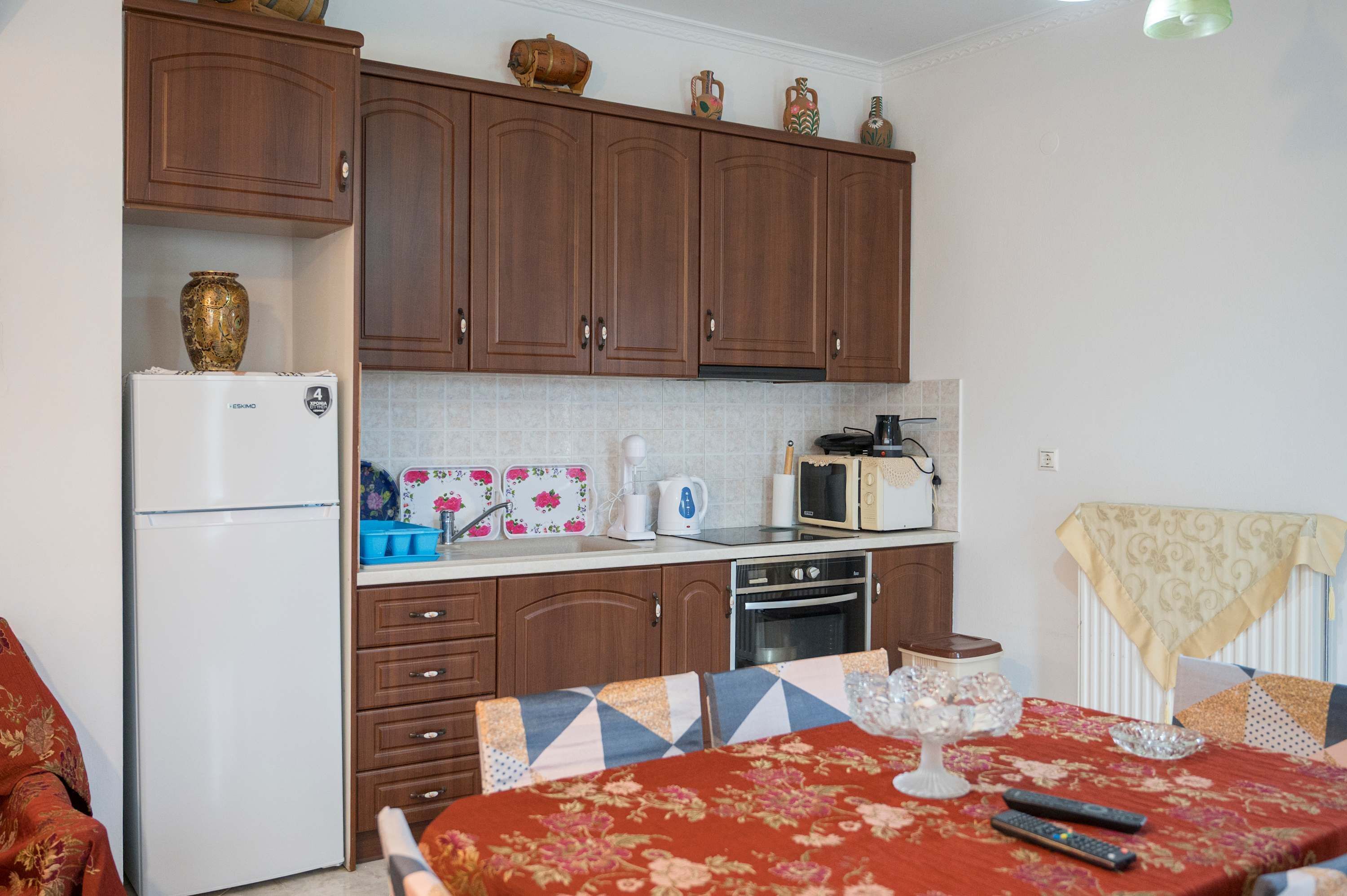 Una cucina compatta con mobili in legno, un frigorifero, un forno a microonde e un'area pranzo con un tavolo apparecchiato per due.
