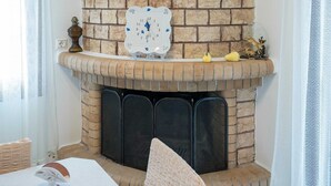 Een kamer met een haard van baksteen, een klok en een tafel met stoelen.