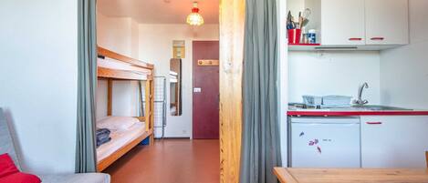 Une chambre d’hôtel compacte comprenant un lit superposé, une petite kitchenette et un coin repas.