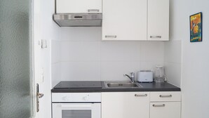 A compact kitchen with white cabinets, a black countertop, a stainless steel range hood, a toaster, and a coffee maker. - Modern 2BR Apartment Long Stay Belvedere (Vienna)