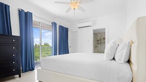 Ein Schlafzimmer mit Bett, Schminktisch, Deckenventilator und Blick auf Grünfläche.