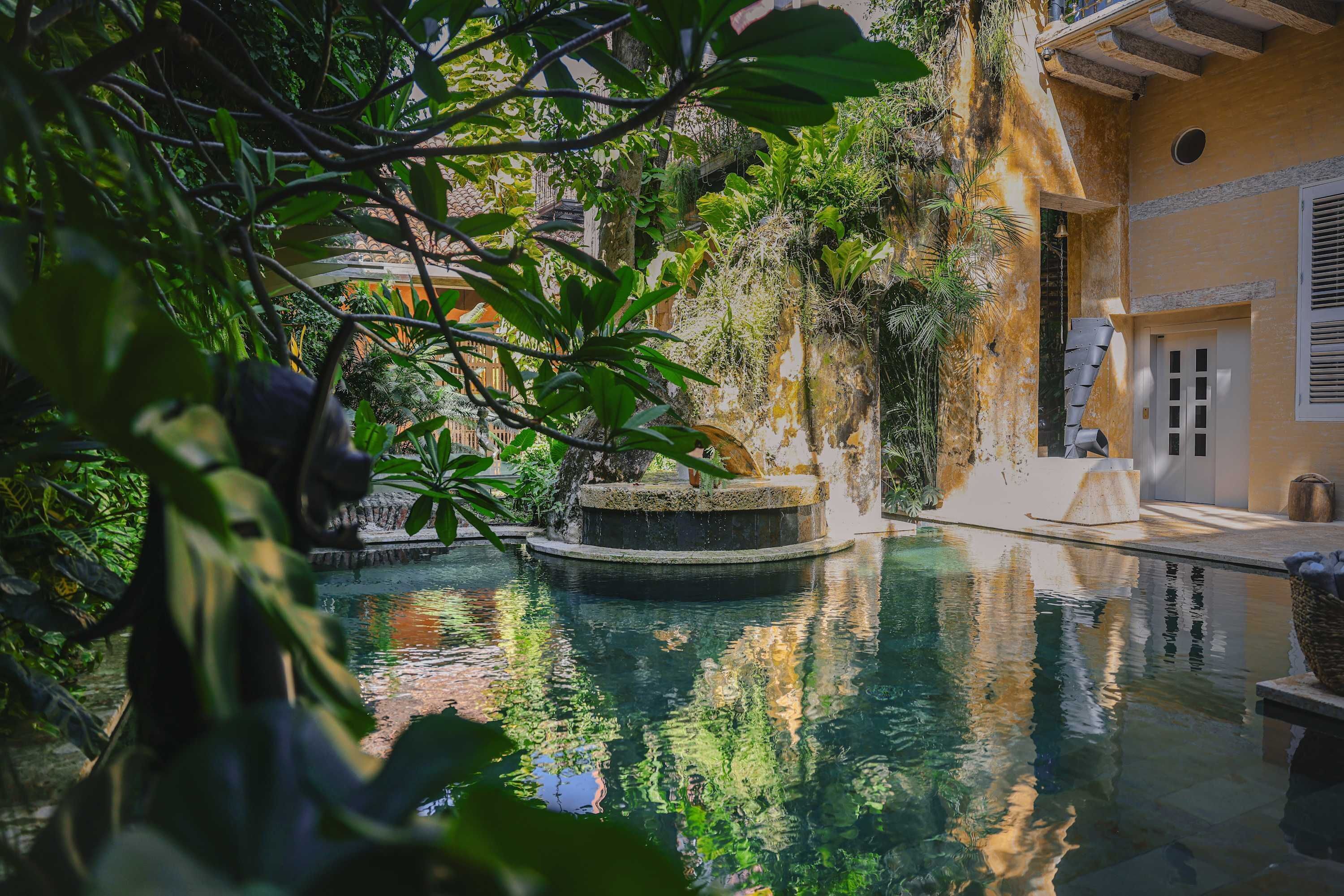 A tranquil indoor pool surrounded by lush greenery and a rustic building with a stone fountain.