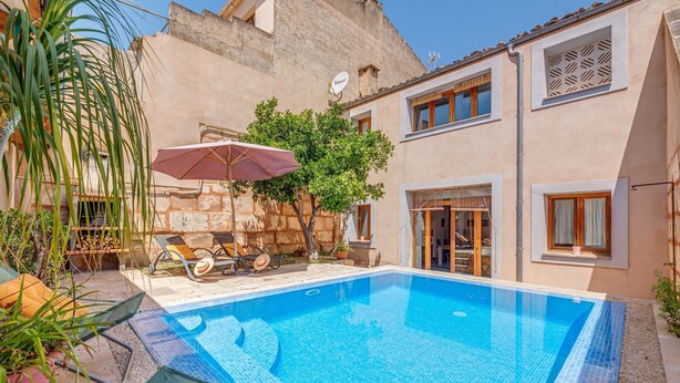 A swimming pool with lounge chairs and umbrellas, a stone wall, and a building with windows and a satellite dish. - Beautiful Home in the Heart of Mallorca with Air Conditioning and Wi-Fi (Petra)