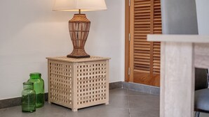 A corner with a woven lamp on a square stool, two green glass bottles, and a wooden door with louvered panels. - Beautiful Home in the Heart of Mallorca with Air Conditioning and Wi-Fi (Petra)