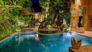 A nighttime pool area with a circular water feature, surrounded by lush greenery and stone architecture. - NOK Private Villa in Cartagena s Walled City (Cartagena)