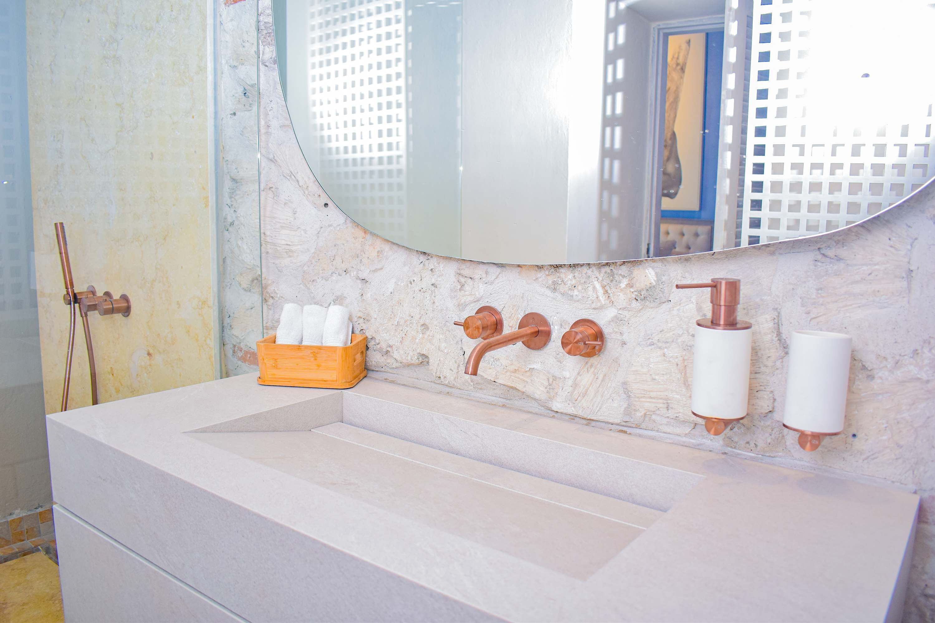 A bathroom with a marble sink, copper faucets, a mirror, and a wooden box with toiletries.
