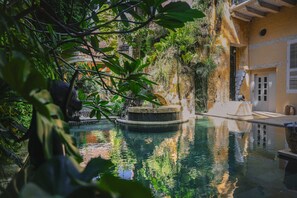 A tranquil indoor pool surrounded by lush greenery and a rustic building with a stone fountain. - NOK Art Suites In Ciudad Amurallada (Cartagena)