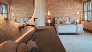Ein Schlafzimmer mit einem großen Bett, einem kleinen Nachttisch, einem Beistelltisch und einem Fenster mit Jalousien.