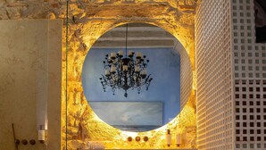 A bathroom with a stone wall, a round mirror, a chandelier, a bathtub, and a shower area. - NOK Bright Suite In Ciudad Amurallada (Cartagena)