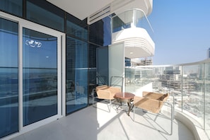 A modern balcony with glass walls, wicker furniture, and a view of the cityscape. - Stayshort - Sleek and Modern Studio in Arjan That Sleeps 2 (Dubai)