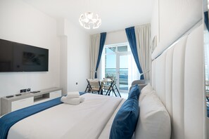 A modern hotel room with a large bed, a desk, and a balcony with curtains. - Stayshort - Sleek and Modern Studio in Arjan That Sleeps 2 (Dubai)
