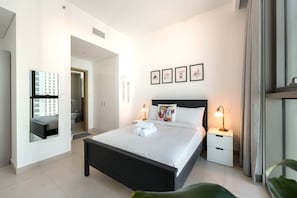 A modern hotel room with a large bed, bedside tables, a mirror, and framed pictures on the wall. - Stayshort - 2 Bed in Downtown Dubai That Sleeps 4 With Canal Views (Dubai)