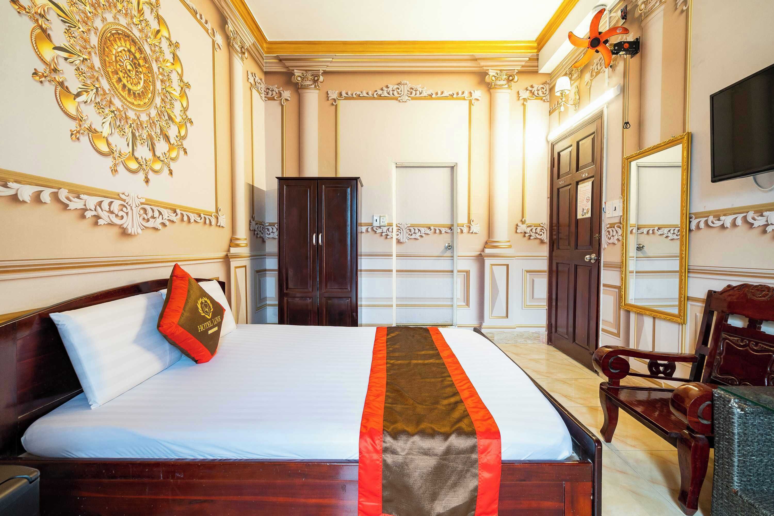 A hotel room with a large bed, a wooden wardrobe, a mirror, and a television on the wall.