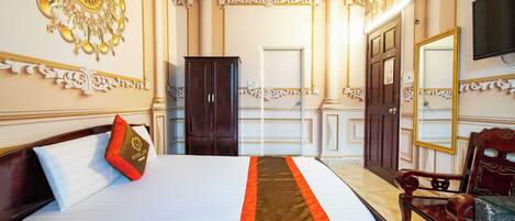 A hotel room with a large bed, a wooden wardrobe, a mirror, and a television on the wall.