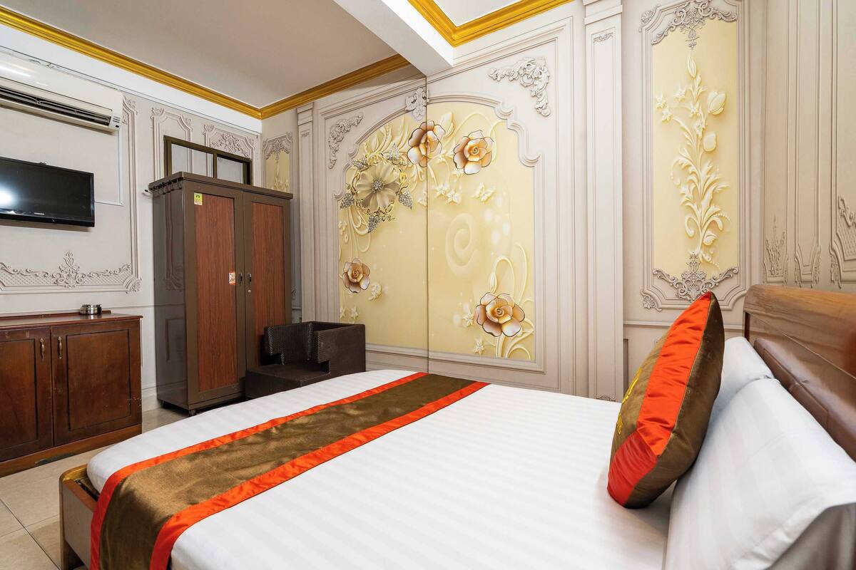 A hotel room with a large bed, a wardrobe, a television, and decorative wall panels.