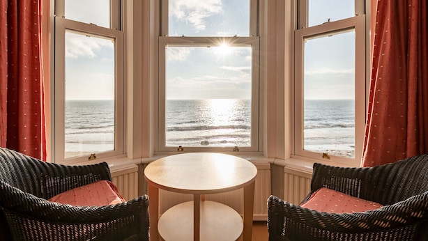A room with a round table and two wicker chairs, a view of the sea through large windows, and red curtains. - Appleton House | Lower Largo (Lower Largo)
