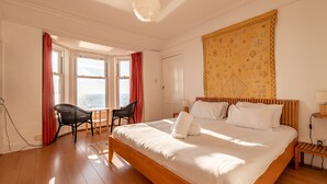 A spacious bedroom with a large bed, a wooden headboard, a view of the sea through the windows, and a tapestry on the wall. - Appleton House | Lower Largo (Lower Largo)