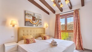 Quarto com uma cama grande, duas mesas de cabeceira, cabeceira, um quadro, janela com cortinas e um candelabro.