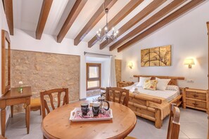 A room with a wooden bed, a dining table with a tray of items, a chandelier, and a stone wall. - Holiday Home "Can Bodeguita" with Wi-Fi, AC, Pool, Balcony & Terrace (Binissalem)