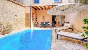 Piscina com espreguiçadeiras e guarda-sol, uma parede de pedra e uma área de refeições com mesa e cadeiras.