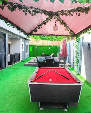 A pool table with a red felt surface, surrounded by artificial green grass. - Luxurious 3-bedroom Apartment in Lagos With Pool Access (Lagos)
