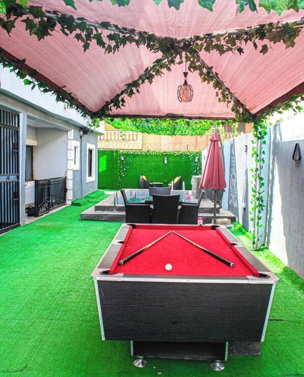 A pool table with a red felt surface, surrounded by artificial green grass. - Luxurious 3-bedroom Apartment in Lagos With Pool Access (Lagos)