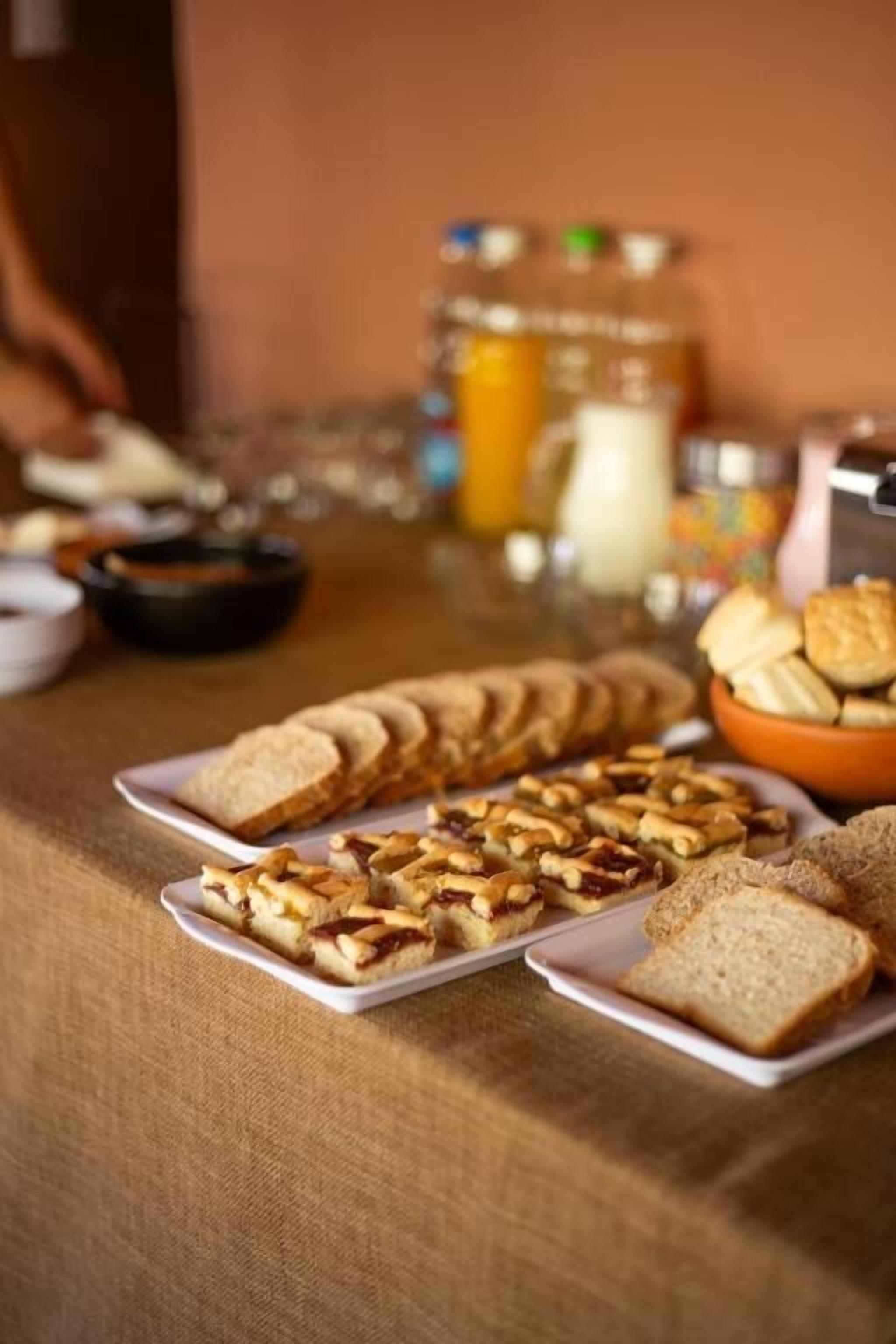A buffet table with sliced bread, pastries, and a pitcher of orange juice.