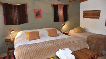 A room with a large bed, two bedside tables, a wooden bench, and a small table with towels and flowers.