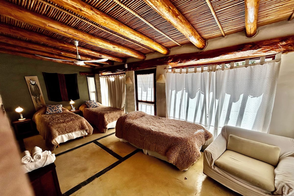 Ein Zimmer mit zwei Betten, einem Schlafsofa, einer Holzbalkendecke und einem großen Fenster mit Vorhängen.