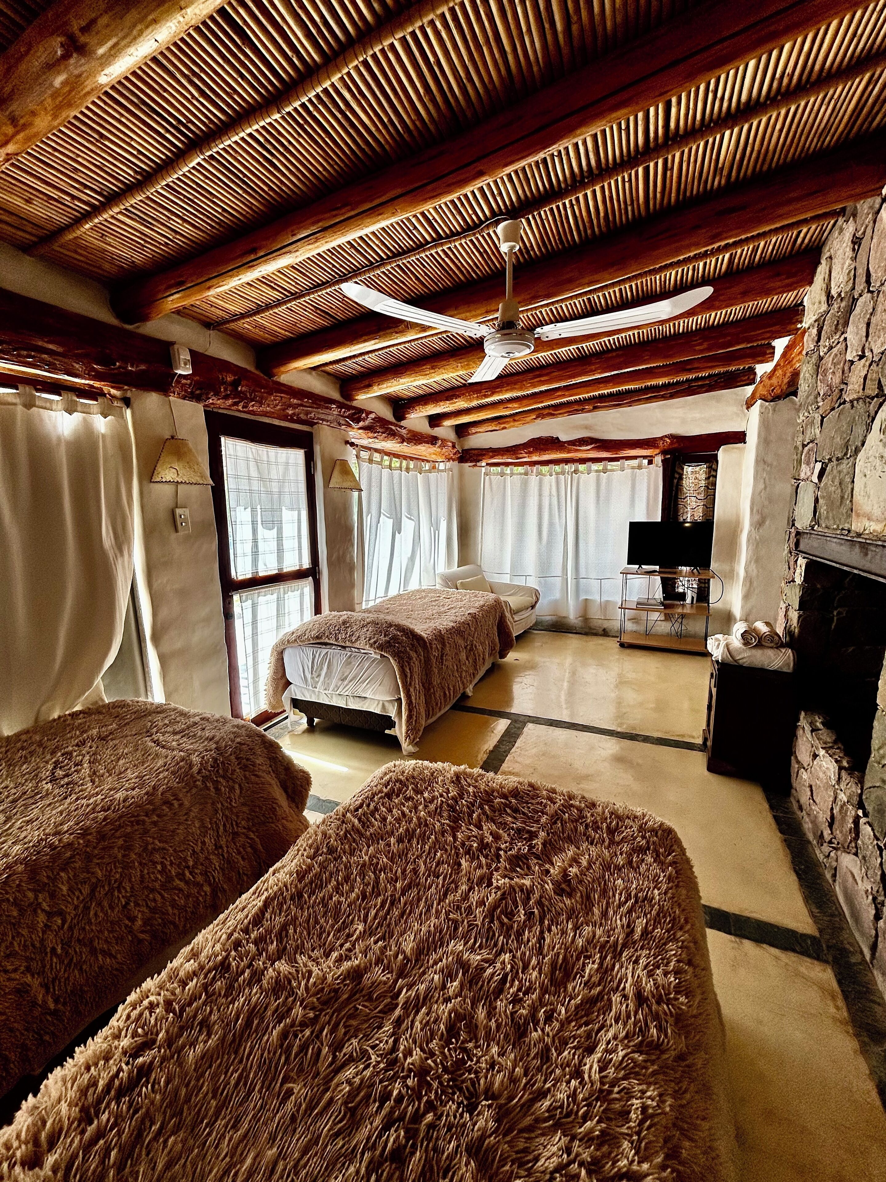 Una habitación acogedora con techo de madera, chimenea y dos camas con ropa de cama mullida.